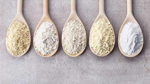 Five wooden spoons with assorted light-colored powders