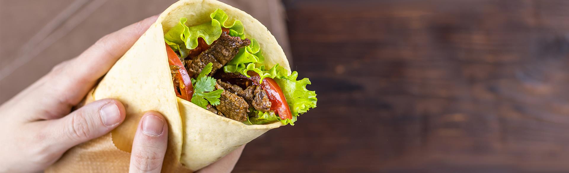 Close-up of a wrap sandwich with lettuce, tomatoes, and grilled meat on a wooden surface